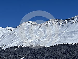 Beautiful sunlight and snow-capped alpine peaks above the Swiss tourist sports-recreational winter resorts