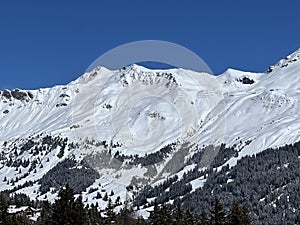 Beautiful sunlight and snow-capped alpine peaks above the Swiss tourist sports-recreational winter resorts