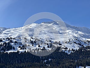 Beautiful sunlight and snow-capped alpine peaks above the Swiss tourist sports-recreational winter resorts