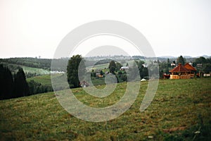 Beautiful sunny meadow with wooden cabins on hills among woods at sunset in mountains. View on evening hills in Carpathian