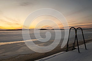 Beautiful sunrise over frozen lake and dock ladder to be used for winter swimming
