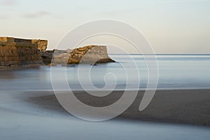 Beautiful sunrise over Pentewan Sands in Cornwall with pastel sky and long exposure ocean