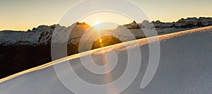 Beautiful sunrise in snowy mountain landscape. Sunbeams illuminating unspoiled powder snow. Alps, Switzerland.