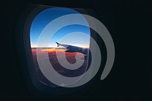 Beautiful sunrise view through the porthole during the flight. Plane wing above the cloudy colorful sunset