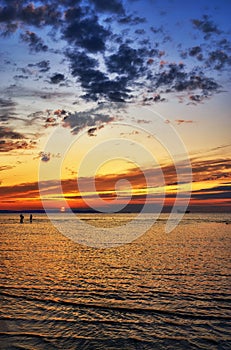 Beautiful sunset on the Baltic Sea beach. People walk in the water and a ship sails in the background