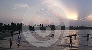 Beautiful sunset on the beach of Arugam Bay, kid with a surfboard, girls playing frisbee