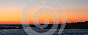 Beautiful sunset on beach in Portugal, with rocks, beach huts and lifebuoys in silhouette