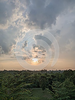 A beautiful sunset behind the rolling clouds in the sky, with a lush green forest as the backdrop