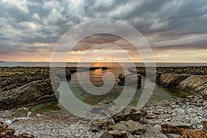 Beautiful sunset on a glass beach by the sea surrounding Sicily and its rocky shores