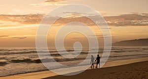 Beautiful sunset on Karon beach. The surf pounds the shore. Dark dim silhouettes of a man and a woman walking arm in arm along sur