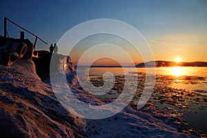 Beautiful sunset on Lake Baikal. On the pier, a man and a woman watch the sunset. Melting ice in the lake.