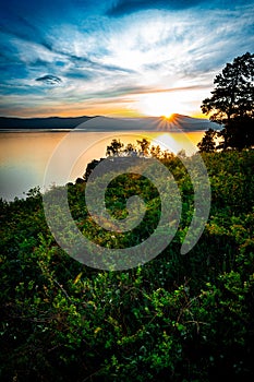 Beautiful sunset landscape on mountain lake with sun hiding behind the mountains