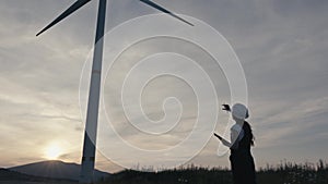 Beautiful sunset landscape where a green energy engineer tests the parameters of a wind turbine to ensure stable and