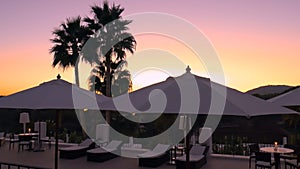 Beautiful sunset in luxury hotel with palms, white umbrellas and chaise lounges. Evening relaxation at spa resort
