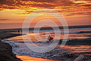 Silhouette of surfer with surfboard walking on the beach in sunset