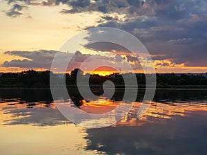 Beautiful sunset over the city horizon with reflection on the calm lake water in a silent summer evening