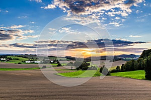 Beautiful sunset over countryside landscape of rolling hills with sun beams piercing sky and lighting hillside