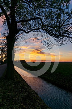 Beautiful sunset over the countryside near Gouda, Holland. Colorful clouds are reflected in the water of a canal.