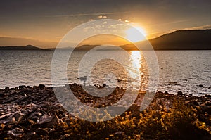 Beautiful sunset over a lake with rocky coast in front and mountains in the background. Lago Maggiore in Italy