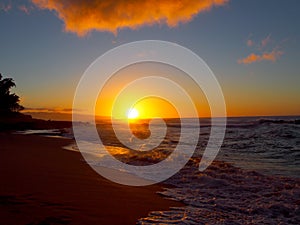 Beautiful Sunset over the ocean and beach with waves moving to shore and foot prints in the sand