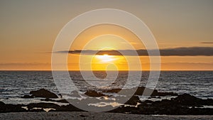 Beautiful sunset over ocean with bright orange sky and shining sun behind cloud on horizon