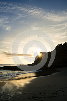 A beautiful sunset over the ocean with a bright sun shining on the water on a rocky beach