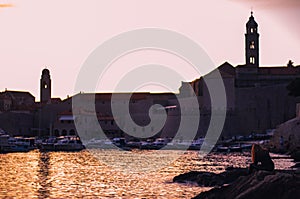 Beautiful sunset over the old town of Dubrovnik. Small local harbour in front of the city, woman in black clothes sitting on a