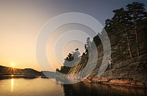 Beautiful sunset rays of sun with clean nordic nature, angler and pine trees on rock in North Europe, Baltic sea, gulf of Finland