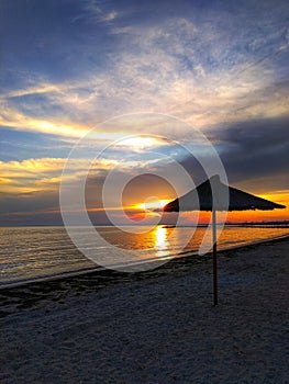 Beautiful sunset on the sandy beach. Straw umbrella by the sea, calm, beautiful natural background. photo