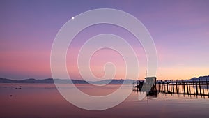 Beautiful sunset scene at a lake with a wooden pier and a house in the distance