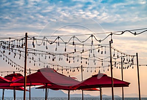 Beautiful sunset scene with top part of many red umbrella beach and party light bulbs hang on the air, colourful sky