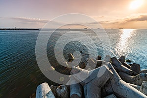 Beautiful sunset seascape. Breakwaters tetrapods ashore of pier. Cargo ships on the horizon. Travel dreams and motivation