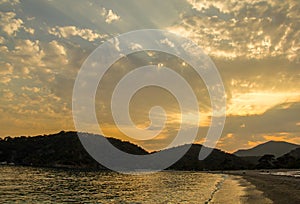 Beautiful sunset at the seaside with mountains on background. The sun breaks through the clouds. A stream of light appears from