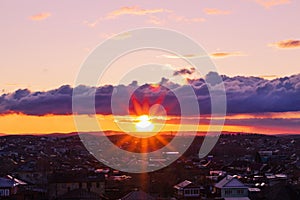 Beautiful sunset sky with small clouds illuminated by the rays of the sun over the silhouette of urban houses. The last rays of