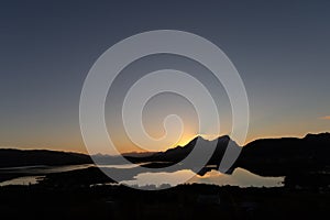 Beautiful sunset with sun setting behind two mountains in Lofoten, Norway