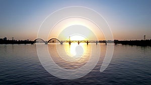 Beautiful sunset, sunrise over the river. Dark silhouette of the arch bridge. Golden twilight, sunlight reflected in water ripples