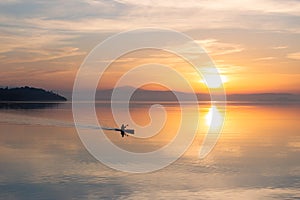 Beautiful sunset at Trasimeno lake with a man on a canoe above perfectly still water