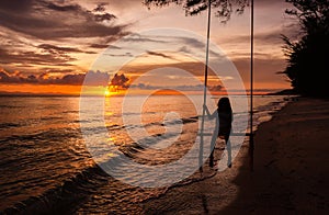 Beautiful sunset tropical beach, The girl is happiness swinging on a swing