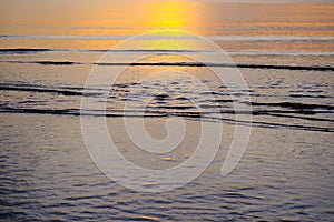 Beautiful sunset view on the beach. Colorful sea beach sunset with golden light reflected on the water surface and soft waves.