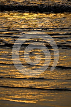 Beautiful sunset view on the beach. Colorful sea beach sunset with golden light reflected on the water surface and soft waves.