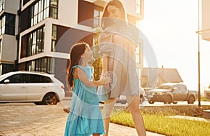 Beautiful sunshine. Young mother with her little daughter walking near the buildings