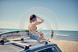 Beautiful surfer girl sitting on the car and getting ready for s