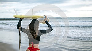 Beautiful surfer girl walking down to the beach for sunset surf session carrying surfboard on head, copy space, fre spce for text