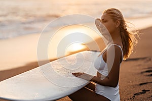 Beautiful surfer woman on the beach at sunset