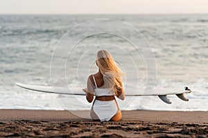 Beautiful surfer woman on the beach at sunset