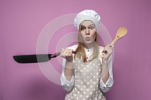 Surprised girl cook in kitchen clothes holds a frying pan and cooks dinner on a pink background, shocked woman housewife with