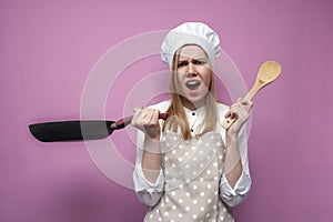 Surprised girl cook in kitchen clothes holds a frying pan and cooks dinner on a pink background, shocked woman housewife with