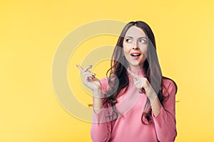 Beautiful surprised woman pointing finger at copy space looking away isolated on yellow background