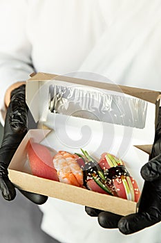 Beautiful sushi in craft packaging for delivery in the hands of a chef. Food delivery. Food at home. Delivery concept.
