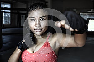 beautiful and sweaty young Asian woman in sport cloths and fighting gloves throwing punch